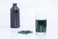 Chlorophyll in glass of water, green pills, bottle on white wooden background Royalty Free Stock Photo