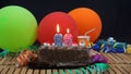 Chocolate birthday 86 cake with candles burning on rustic wooden table with background of colorful balloons