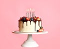 Chocolate Birthday sweet cake with fresh fruits, berries and lighted candles on top over a popular light pink