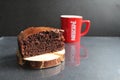 Chocolate brownie pie on a wooden stand log cabin back in the background is a red mug a Cup of tea coffee milk on a black backgrou