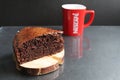 Chocolate brownie pie on a wooden stand log cabin back in the background is a red mug a Cup of tea coffee milk on a black backgrou