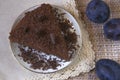 Chocolate brownie with pieces of chocolate in a white plate on a white napkin and three plums Royalty Free Stock Photo