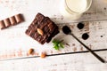 Chocolate brownies with melted chocolate topping, almond and leaves mint with glass of milk on table