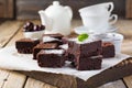 Chocolate brownies with powdered sugar and cherries on a dark wooden background.