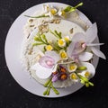 Chocolate cake decorated with flowers and poured white icing on black stone background. Top view. Flat lay