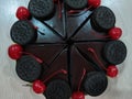 Chocolate cake, divided into pieces, decorated with Oreo and red cherries.