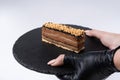 Chocolate cake with peanuts and caramel on round black rock stand in hands on white background. Tasty dessert concept