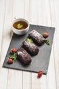 Chocolate cakes with strawberry filling on a black slate board with a cup of tea on a white wooden background Royalty Free Stock Photo