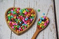 Chocolate candies covered in colored sugar in a wooden heart-shaped bowl and a wooden spoon. Royalty Free Stock Photo