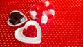 Chocolate candies in heart shaped plate, white and red roses on red background Royalty Free Stock Photo