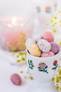 Chocolate candy colored Easter eggs in ceramic cup burning candle, small flowers