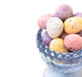 Chocolate candy speckled multicolored Easter eggs in pastel colors in blue crystal cup on white background