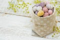 Chocolate candy Multi-Colored Small Quail Easter Eggs Pastel Colors in Linen Sack White Wood Table Yellow Spring Flowers