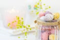 Chocolate Candy Multi-Colored Small Quail Easter Eggs Pastel Colors in Vintage Glass Jar on White Wood Table Yello Flowers