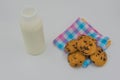 Chocolate chip cookies on a cloth and Bottle of milk on white background.