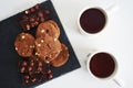 Chocolate cookies with chocolate slices and nuts on a dark stand next to two cups of tea Royalty Free Stock Photo