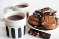 Chocolate cookies with chocolate slices and nuts on a plate next to two cups of tea Royalty Free Stock Photo