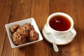 Chocolate cookies with walnuts and raisins in a square bowl and a cup of black tea on a wooden table. Royalty Free Stock Photo