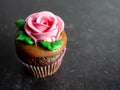 Chocolate cupcake with chocolate frosting decorated with a large pink rose and green leaves sitting on a black slate background Royalty Free Stock Photo