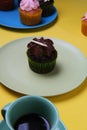 Chocolate cupcake on a grey plate on a yellow surface with a cup of coffee and other cupcakes Royalty Free Stock Photo