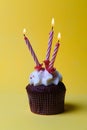 Chocolate cupcake with white cream and three candles on a yellow background Royalty Free Stock Photo