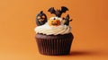 a chocolate cupcake with white icing, topped with small Halloween decorations including pumpkins, a bat, and a ghost