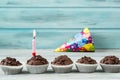 Chocolate cupcakes with candle on wooden table against blue background and party cap