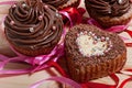 Chocolate cupcakes with chocolate cream and cupcake in the shape of heart, decorated with ribbon, on a wooden background. Royalty Free Stock Photo