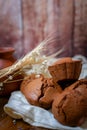 Chocolate cupcakes lie on a white cloth decorated with wheat