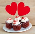 4 chocolate cupcakes with white frosting and red sprinkles under 2 red hearts