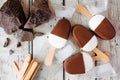 Chocolate dipped vanilla ice cream bars on a rustic white wood table