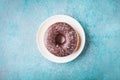 Chocolate donut or doughnut in plate on turquoise table top view. Flat lay.