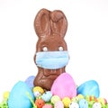Chocolate Easter bunny, surrounded by Easter eggs, wearing a medical face mask for protection to the coronavirus