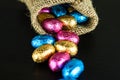Chocolate Easter eggs in colorful foil scattered from jute bag