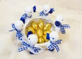Chocolate Easter eggs in golden cover in white with blue round vase with ducks figures