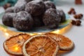 Chocolate gingerbread sprinkled with powdered sugar on a plate with turquoise leaves, dried oranges and garland