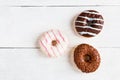 Chocolate and glazed donuts, pink, white, brown on wooden table, top view