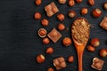 Chocolate with hazelnuts and a wooden spoon with cocoa on a dark background, surrounded by nuts in the shell and peeled