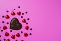 Chocolate heart and lots of shiny candy in the shape of hearts wrapped in foil on a pink background