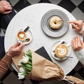 Hands of young couple eating dessert and holding hands on table with coffee, gift box and flowers Royalty Free Stock Photo