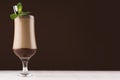 Chocolate milk cocktail in goblet with fresh green mint and silver spoon in elegant dark brown bar interior, copy space. Royalty Free Stock Photo