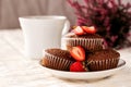 Chocolate muffins with strawberries on a saucer with a white cup of coffee.