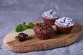 Chocolate muffins on a wooden board, strewed with icing sugar.