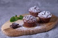 Chocolate muffins on a wooden board, strewed with icing sugar. Homemade baking.