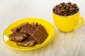 Chocolate pieces in saucer, coffee beans in cup on wooden table Royalty Free Stock Photo