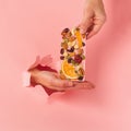 Chocolate pink bar holds a female hand on a pink background burst paper hole. Food concept art. Square frame Royalty Free Stock Photo