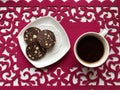 Chocolate sausage, cut in rings, lies on a saucer. On a red napkin. Nearby is coffee in a white mug.