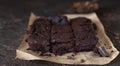 Chocolate spongy brownie cakes on brown baking paper with pieces of dark chocolate and cocoa powder, brown background