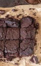 Chocolate spongy brownie cakes on brown baking paper with pieces of dark chocolate and cocoa powder, brown background