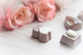 Chocolate sweets and pale roses on wooden table, toned